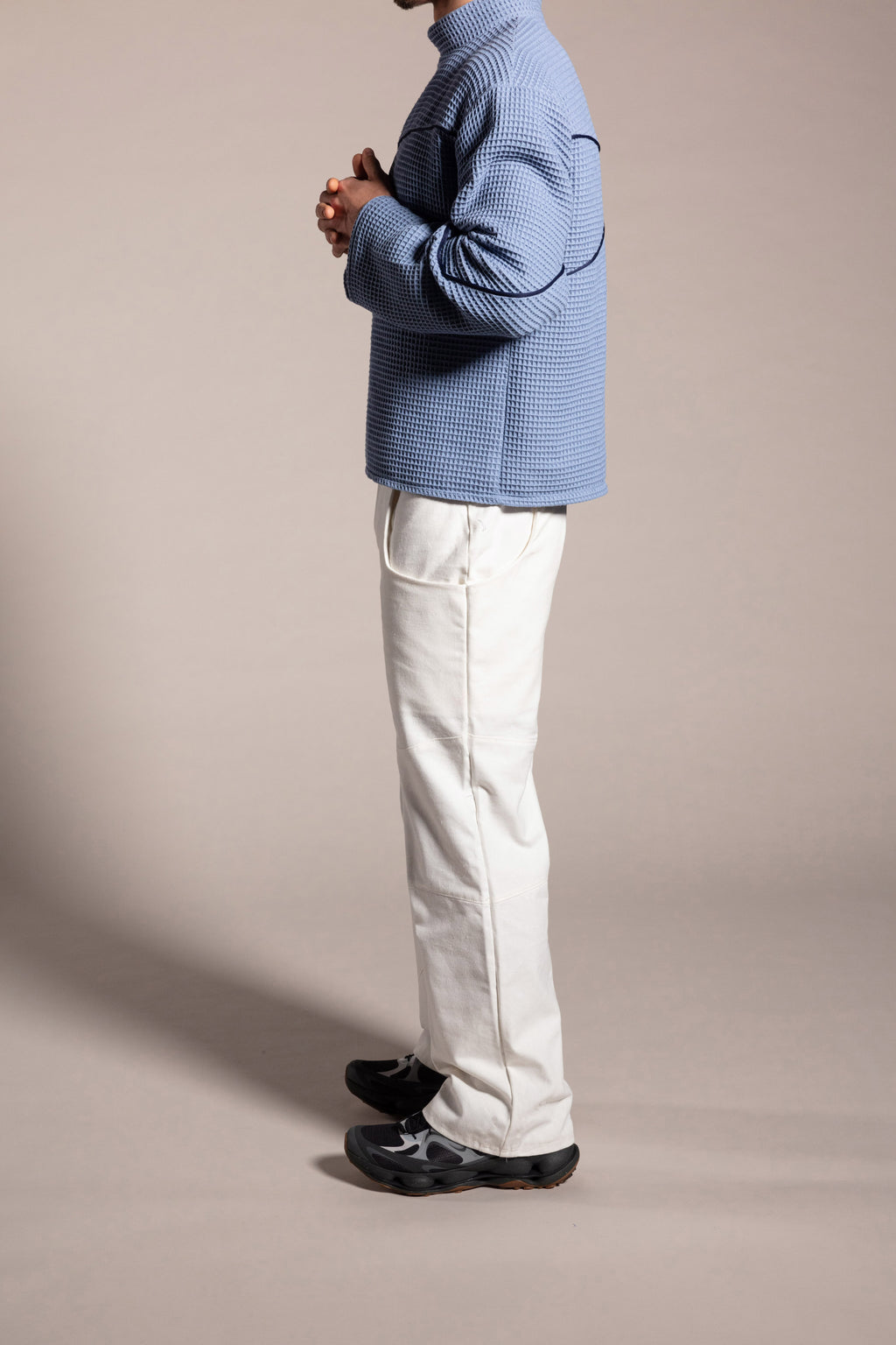 Person wearing a blue textured sweater and white pants against a beige background