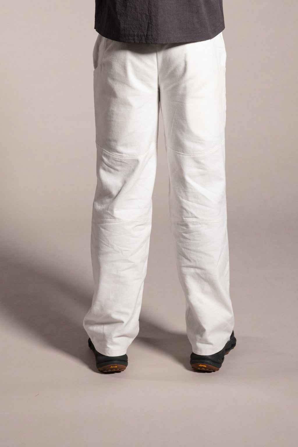 Person wearing a dark shirt and white pants standing against a plain background