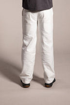 Person wearing a dark shirt and white pants standing against a plain background